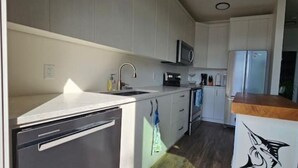 A modern kitchen with white cabinets, a microwave, a refrigerator, and a wooden countertop.