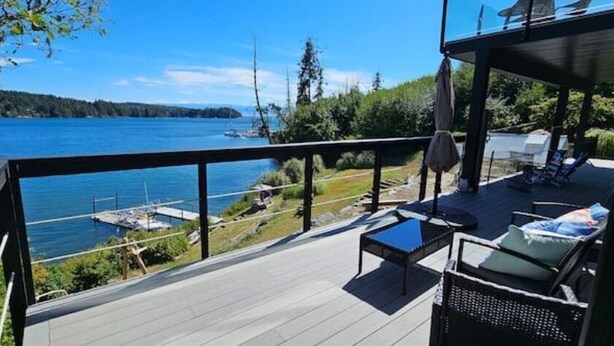 A deck with a view of a lake, outdoor furniture, and a dock.