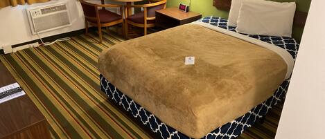 Una habitación de hotel con cama, una mesita redonda con sillas, una lámpara y un equipo de aire acondicionado.