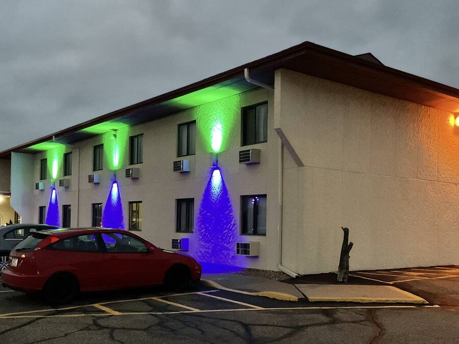 A hotel with multiple floors, air conditioning units, and a parking lot with several cars.