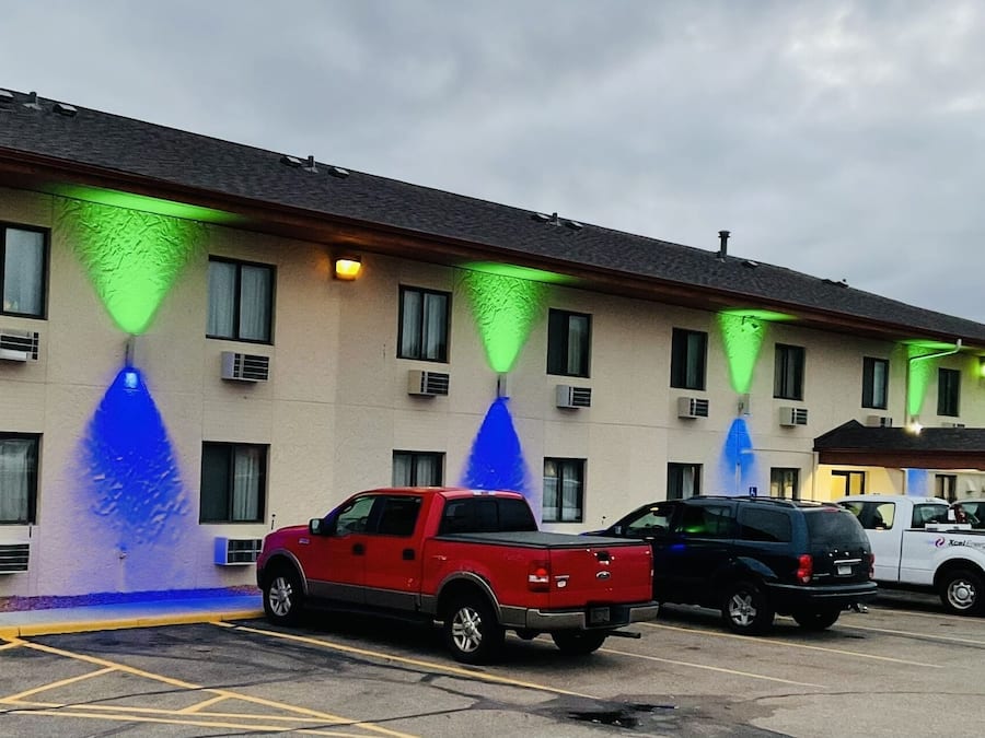 Un hotel con aparcamiento, varios vehículos e iluminación verde en la fachada.
