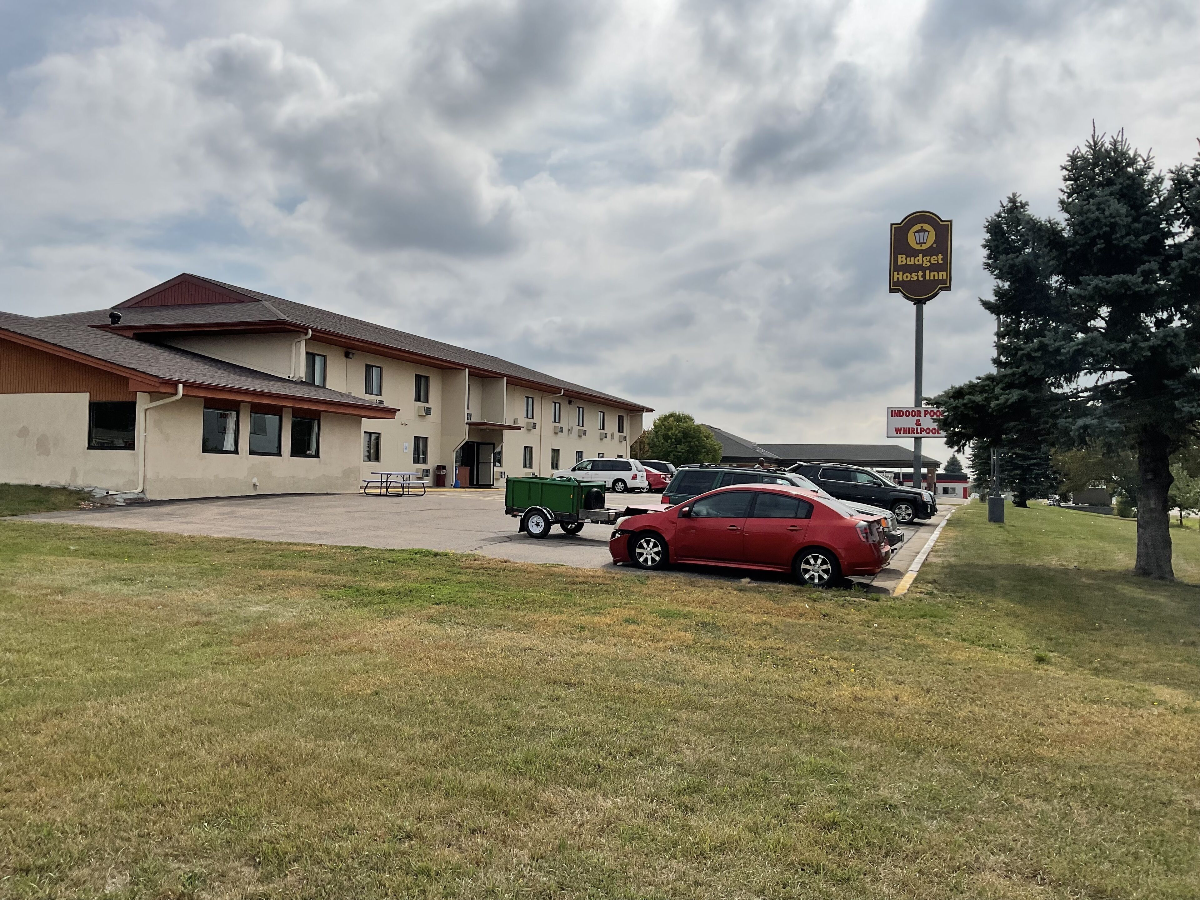Un motel con estacionamiento, un contenedor de basura verde y un letrero que dice 'Budget Lost Inn'.