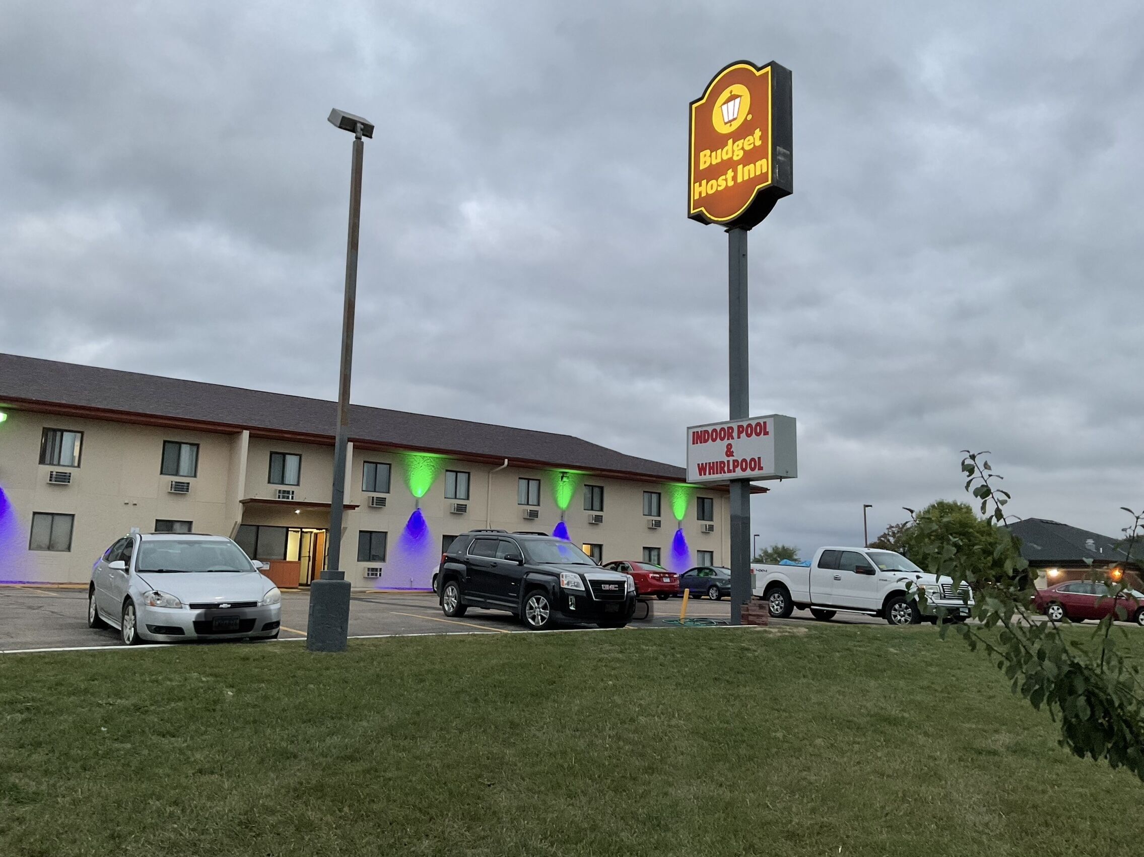 A Budget Host Inn with an indoor pool and whirlpool, parking lot, and a building with multiple windows.