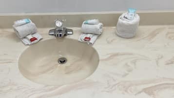 Ein Waschbecken mit Marmorplatte, einem Wasserhahn und drei Handtüchern mit Toilettenartikeln an der Wand darüber.
