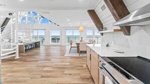 A modern kitchen with a large island, wooden flooring, and a view to the outside.