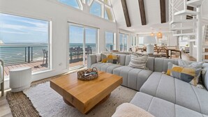 A spacious living area with a large sofa, a wooden coffee table, and a view of the ocean through large windows.