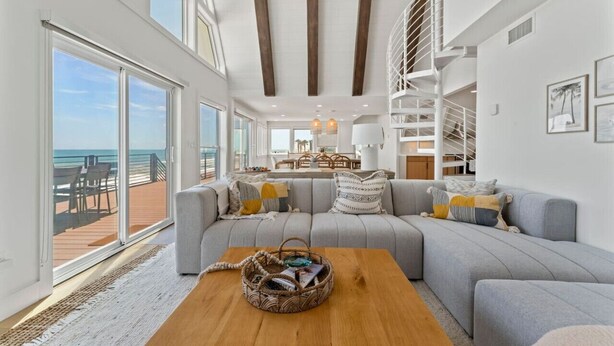 A spacious living area with a large gray sectional sofa, a wooden coffee table, and a view of the ocean through large windows.