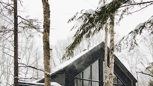 A modern log cabin with large windows and a covered porch, surrounded by snow and trees. - Chalet Metsa Tremblant (Lac-Supérieur)