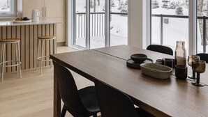 A modern kitchen with large windows, a wooden dining table, and black chairs. - Chalet Metsa Tremblant (Lac-Supérieur)