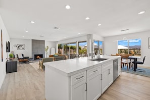 A modern kitchen with a large island, a dining area with a view, and a cozy seating area with a fireplace. - Stunning Desert Getaway w/ Ice Bath & Pool! (Bermuda Dunes)