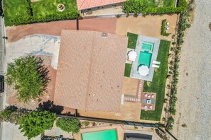 Una vista aerea di una proprietà con un'ampia zona patio, una piscina e un piccolo giardino.