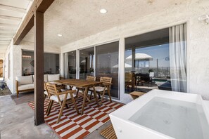 Un'ampia area patio con tavolo e sedie in legno, una grande porta scorrevole in vetro che dà su un patio esterno e una vasca idromassaggio.