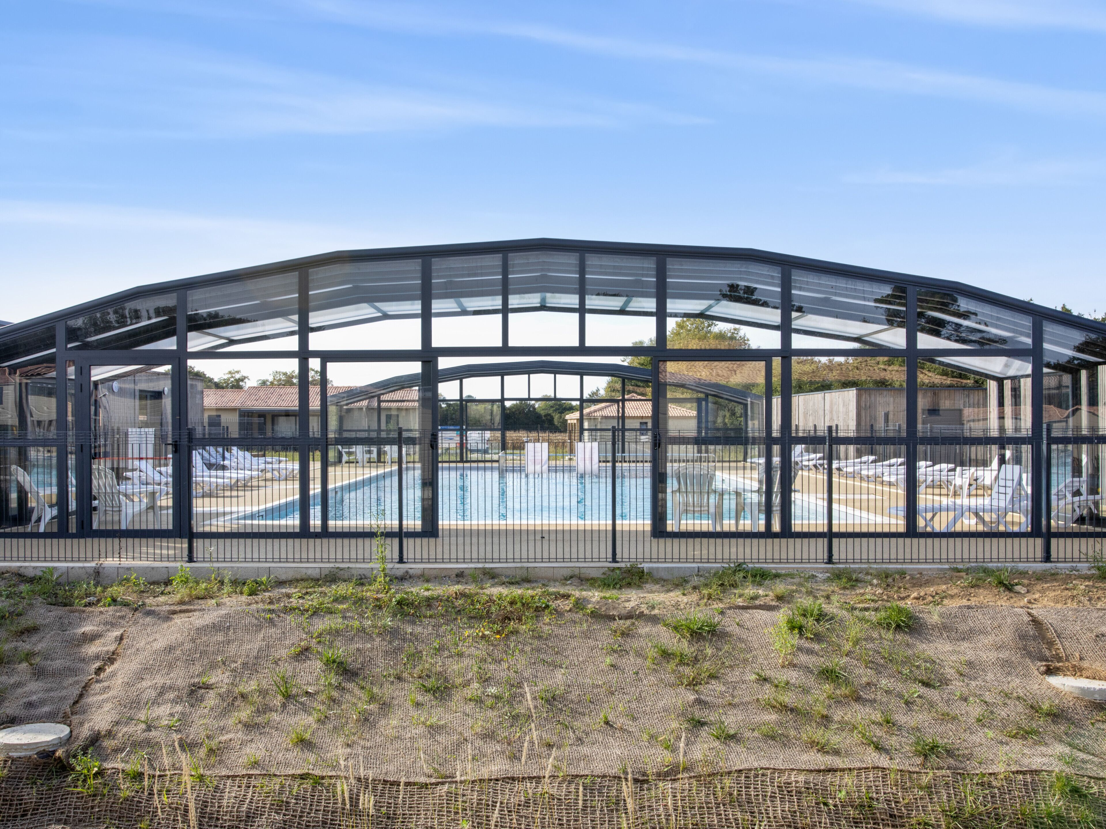 A large, open-air structure with a glass roof, likely a greenhouse or conservatory, overlooking a swimming pool area.