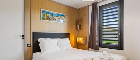 Habitación de hotel con cama, un cuadro en la pared, una ventana con persianas, una mesita de noche con lámpara y un teléfono.