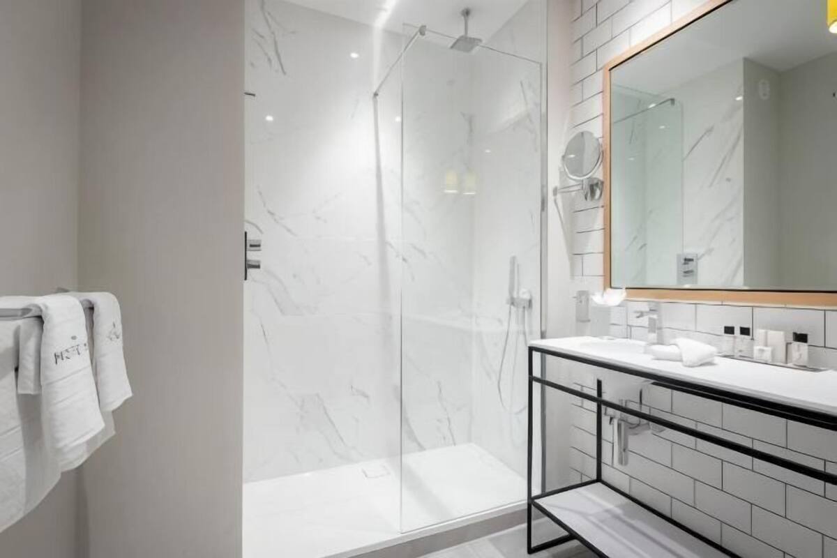 A modern bathroom with a glass-enclosed shower, a white marble wall, and a large mirror.