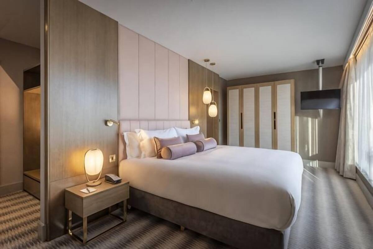 A hotel room with a large bed, bedside tables, a TV, and a wardrobe.