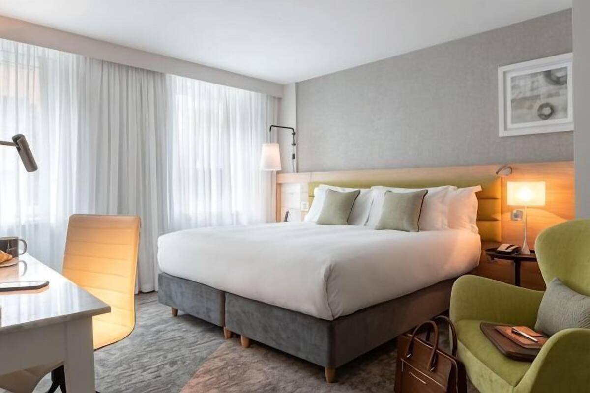 A hotel room with a bed, a desk, a chair, a lamp, and a window with curtains.
