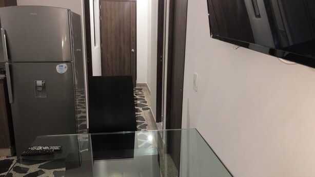 Un couloir étroit avec un réfrigérateur, un meuble noir et une table en verre.
