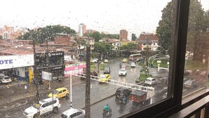 Une rue animée en milieu urbain, avec différents véhicules, des bâtiments et une vue dégagée sur le paysage urbain, visible à travers une fenêtre couverte de gouttes de pluie.