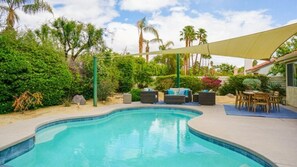 A swimming pool with a curved edge, surrounded by outdoor furniture and a shaded area. - Hidden Gem in Rancho Mirage (Rancho Mirage)