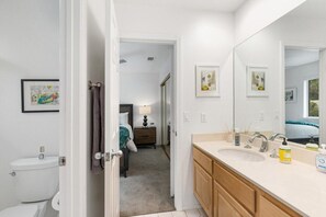 A modern bathroom with a large mirror, a sink, and a toilet. There is a door leading to a bedroom with a bed and a nightstand. - Hidden Gem in Rancho Mirage (Rancho Mirage)