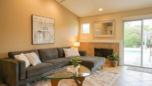 A living room with a sofa, a glass coffee table, a fireplace, and a large window. - Hidden Gem in Rancho Mirage (Rancho Mirage)