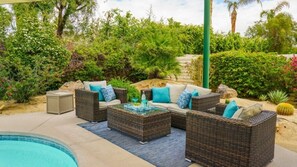 An outdoor seating area with wicker furniture and cushions, a glass-top coffee table, and a pool in the background. - Hidden Gem in Rancho Mirage (Rancho Mirage)