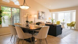 A modern living room with a dining area, featuring a large window, a sofa, a coffee table, and a dining table with chairs. - Hidden Gem in Rancho Mirage (Rancho Mirage)