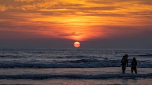 Un coucher de soleil sur l’océan, avec des personnes debout sur la plage.