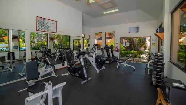 Ein Fitnessstudio mit unterschiedlichen Trainingsgeräten, großen Fenstern und einem Deckenventilator.