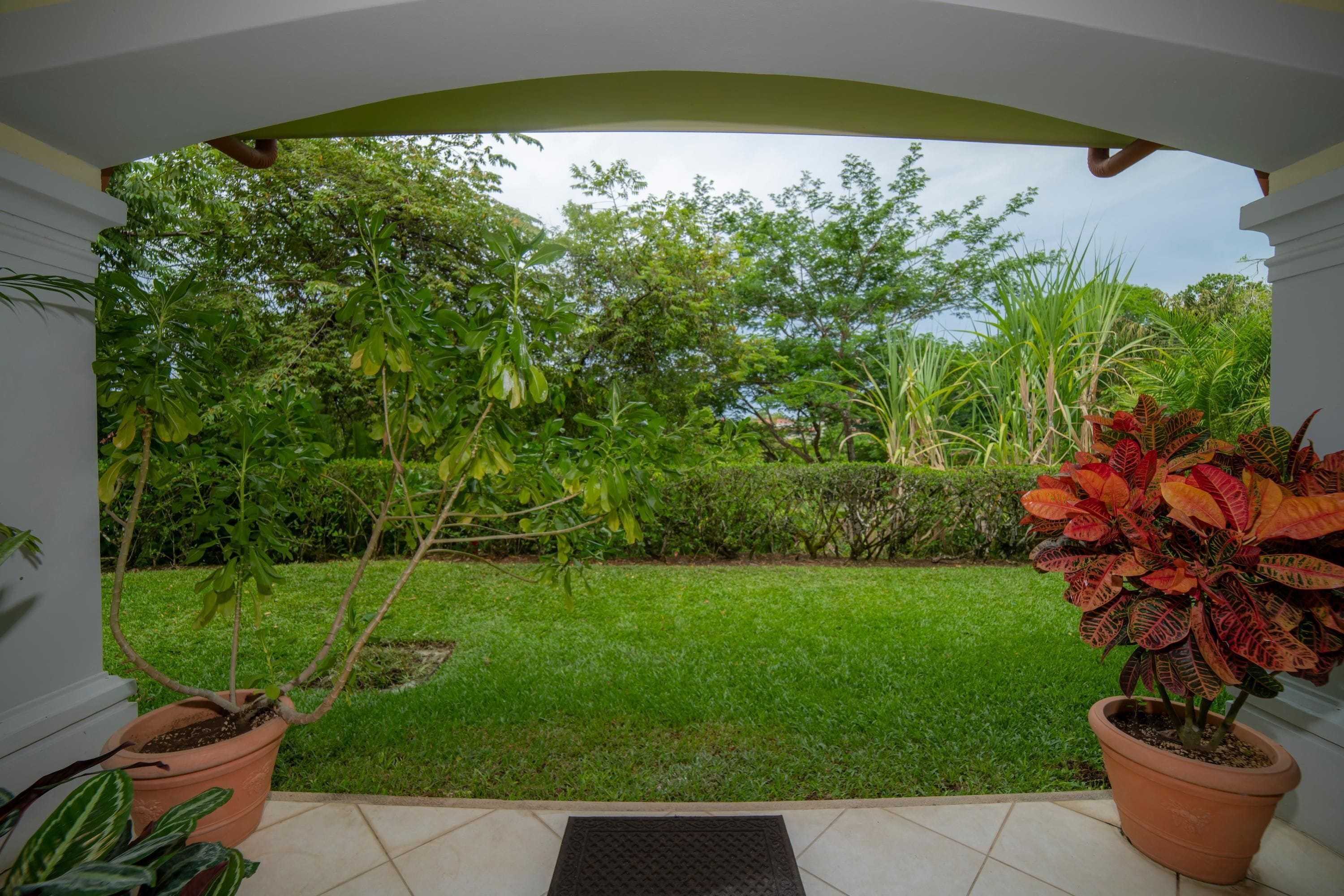 Un patio techado con vistas a un césped cuidado y diversas plantas en macetas.