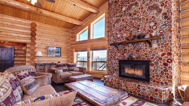 L’intérieur d’une cabane en rondins, avec une cheminée en pierre, des meubles en bois et de grandes fenêtres.
