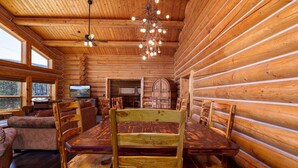 L’intérieur d’une cabane en rondins, avec une table à manger, des chaises, un téléviseur et une cheminée.