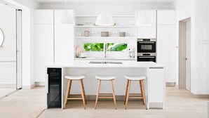 A modern kitchen with white cabinetry, a central island with stools, a built-in oven, and a dishwasher. - Porters Place 13: A one-of-a-kind experience await (Porters)