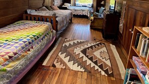Ein gemütliches Schlafzimmer im Dachgeschoss mit schrägen Wänden, Holzboden, einem großen Fenster und einem Bücherregal.