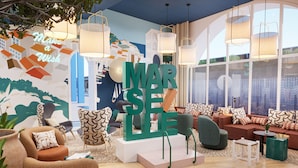 A modern living room with a large 'MARSEILLE' sign, comfortable seating, and large windows.