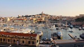 A marina with numerous boats docked, a prominent hilltop structure, and a historic building with arched windows. - Près du Vieux Port | La Joliette | T2 moderne 4p (Marseille)