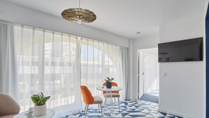 A modern living room with a geometric patterned floor, a round table with chairs, a sofa, a potted plant, and a TV mounted on the wall. - Près du Vieux Port | La Joliette | T2 moderne 4p (Marseille)