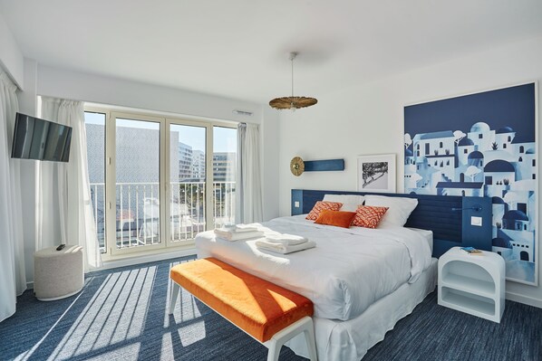 Una habitación de hotel moderna con una cama grande, un banco, un televisor y un balcón con vista a la ciudad.
