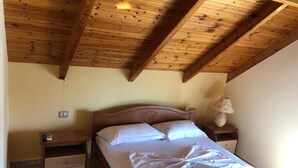 Une chambre avec un plafond en bois, un lit recouvert de draps blancs, une table de chevet avec une lampe et une prise électrique au mur.