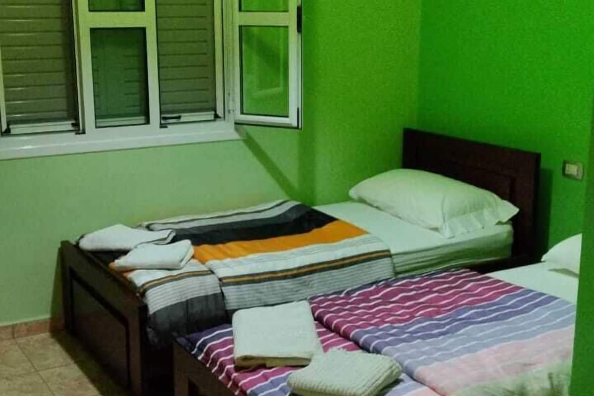 A room with two beds, a window with shutters, and a green wall.