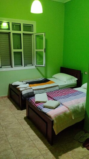 Een kamer met twee bedden, een raam met luiken en een groene wand.