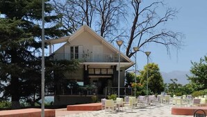 Un bâtiment doté d’un toit plat et d’un balcon, entouré d’une zone pavée avec des chaises et des tables.