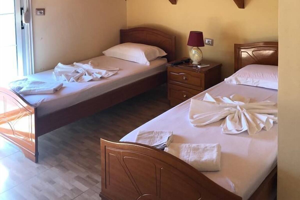 A room with two wooden beds, a nightstand with a lamp, and a wooden ceiling.