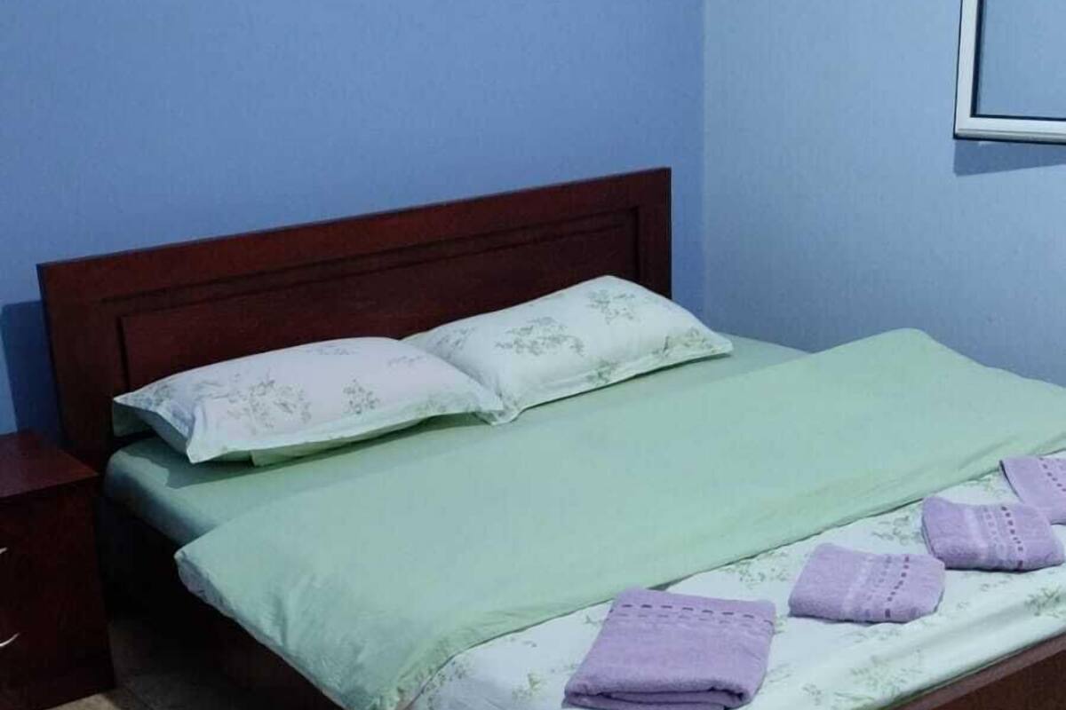 A single bed with a wooden frame, green bedding, and a nightstand to the left.
