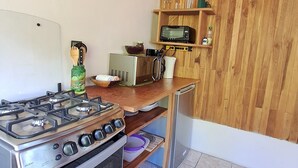 Cocina compacta con estufa a gas, horno, armarios de madera, microondas y una repisa con utensilios de cocina.