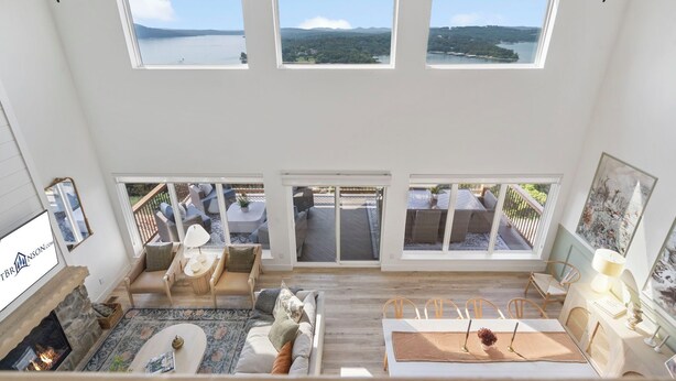 A spacious living room with a fireplace, large windows, and a view of a lake and mountains. - Private Hot Tub, Stunning Decor & Panoramic Lake Views with Free SDC Tickets (Kimberling City)
