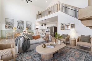 A spacious living room with a high ceiling, a dining area, and a kitchen. There is a staircase connecting two levels.