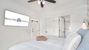 A bedroom with a bed, a ceiling fan, a wall-mounted TV, and a door with a towel rack. - Private Hot Tub, Stunning Decor & Panoramic Lake Views with Free SDC Tickets (Kimberling City)