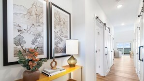 A hallway with artwork, a vase with flowers, a lamp, and a bookshelf. - Private Hot Tub, Stunning Decor & Panoramic Lake Views with Free SDC Tickets (Kimberling City)